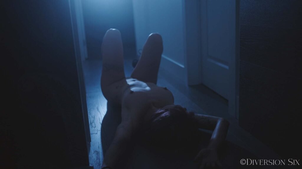 A nude model Ady in a dark hallway with bright light in the background,