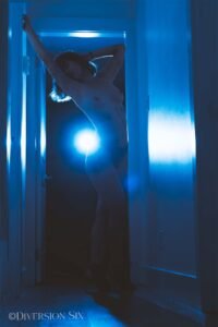 a nude woman standing in a dark hallway with a bright spotlight behind her.
