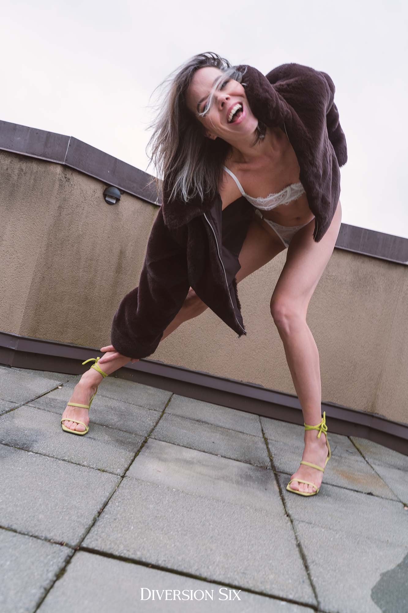 a woman wearing a fur coat and high heels in an edgy fashion pose bending down toward the camera